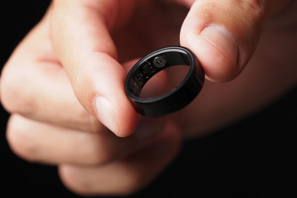 A black smart ring with visible inner biometric sensors held by a person, illustrating wearable health technology used for continuous tracking.