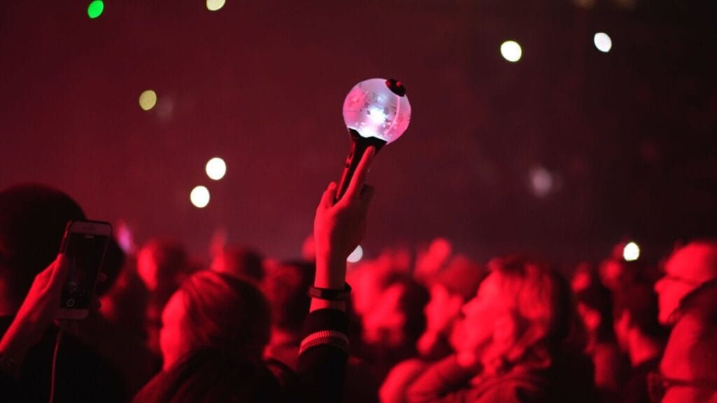 Silhouette of a fan raising a glowing K-pop light stick at a concert with red lighting